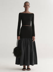 Woman wearing a black off-shoulder top and long skirt with a black feathered bag on a white background