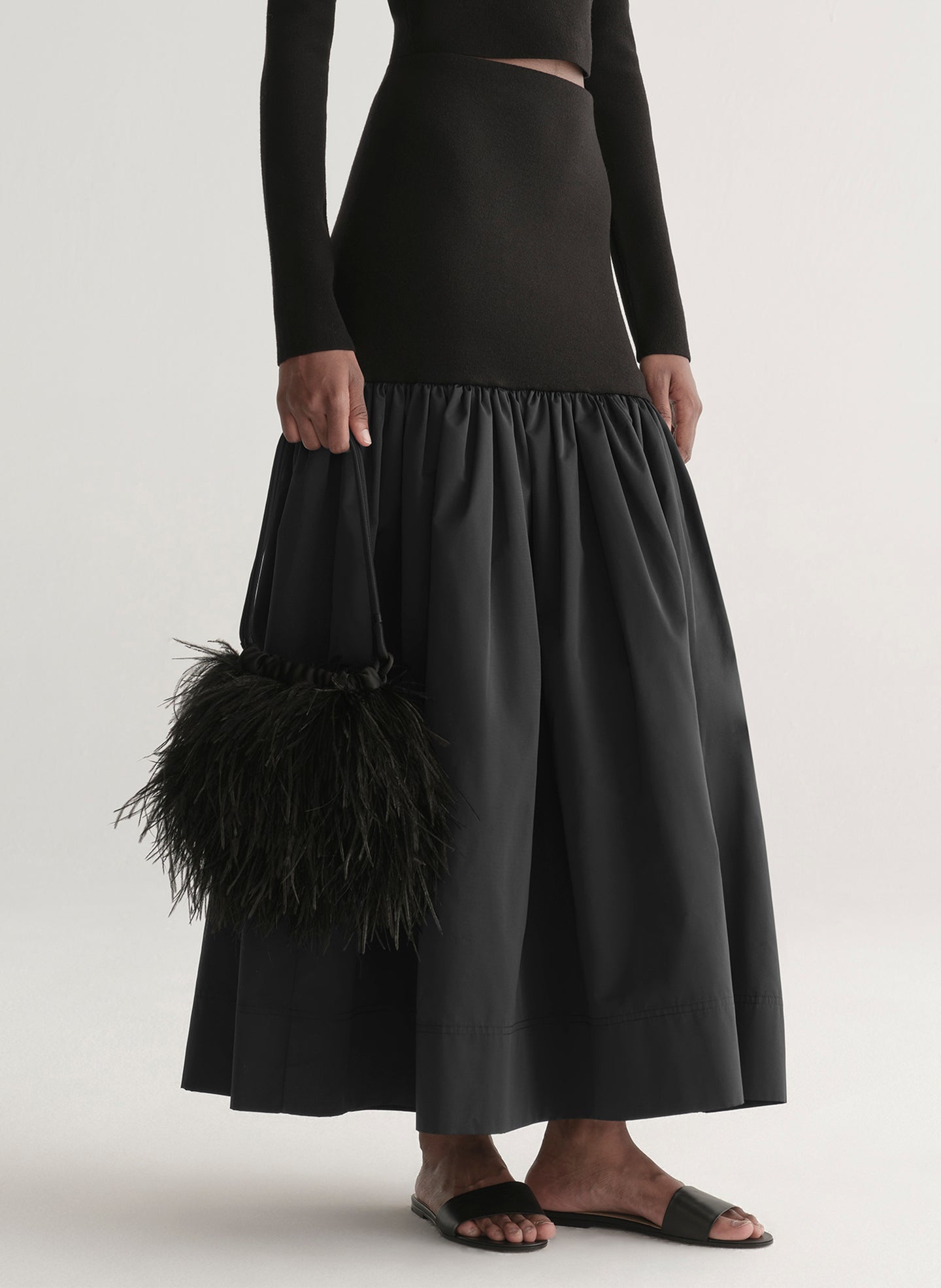 Woman wearing a black off-shoulder top and long skirt with a black feathered bag on a white background
