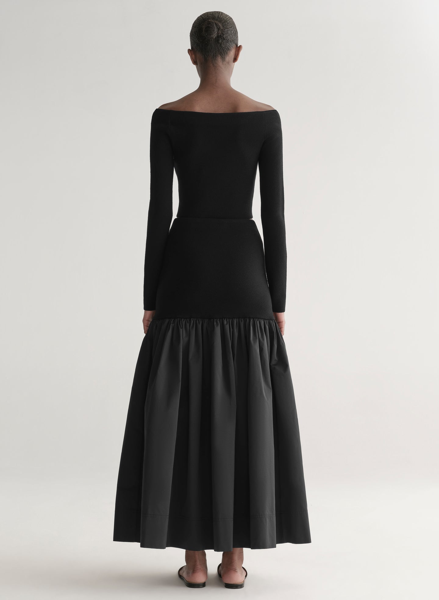 Woman wearing a black off-shoulder top and long skirt with a black feathered bag on a white background