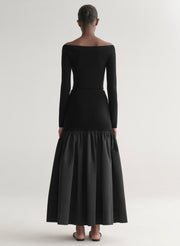 Woman wearing a black off-shoulder top and long skirt with a black feathered bag on a white background