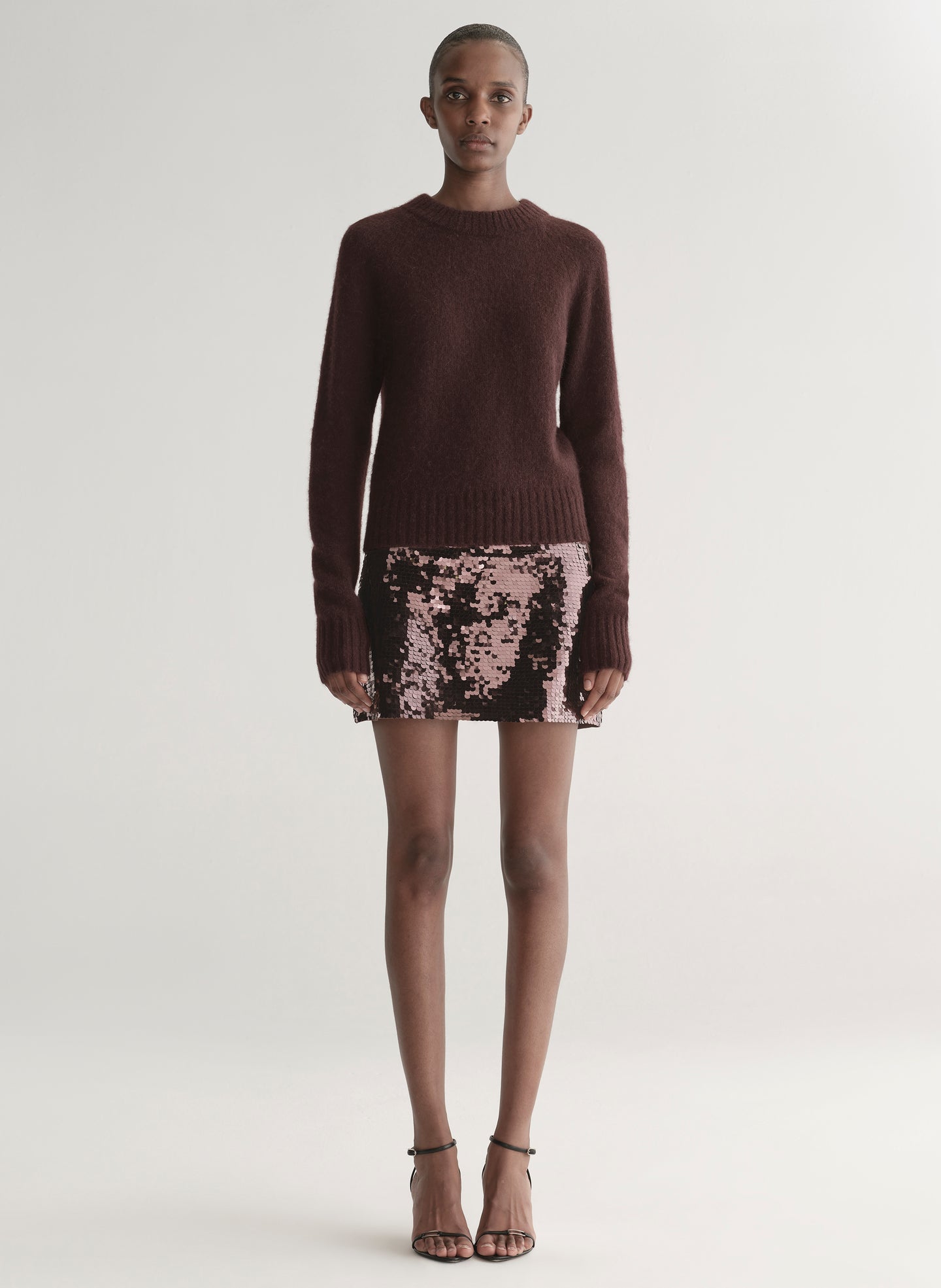 Person wearing a brown sweater and sequin skirt on a white background