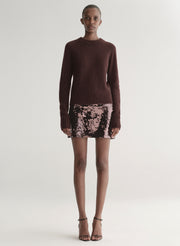 Person wearing a brown sweater and sequin skirt on a white background