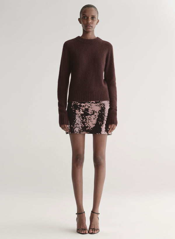 Person wearing a brown sweater and sequin skirt on a white background