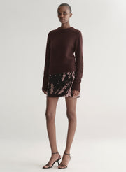 Woman wearing a dark brown sweater dress with sequin skirt on a white background