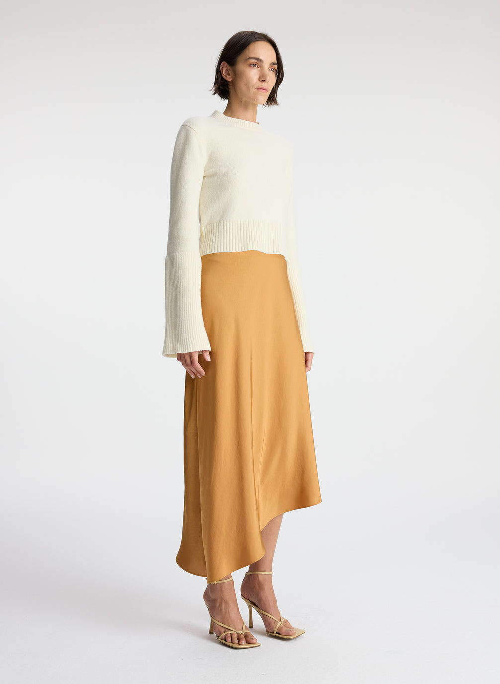side view of woman wearing white sweater and brown satin asymmetric midi skirt