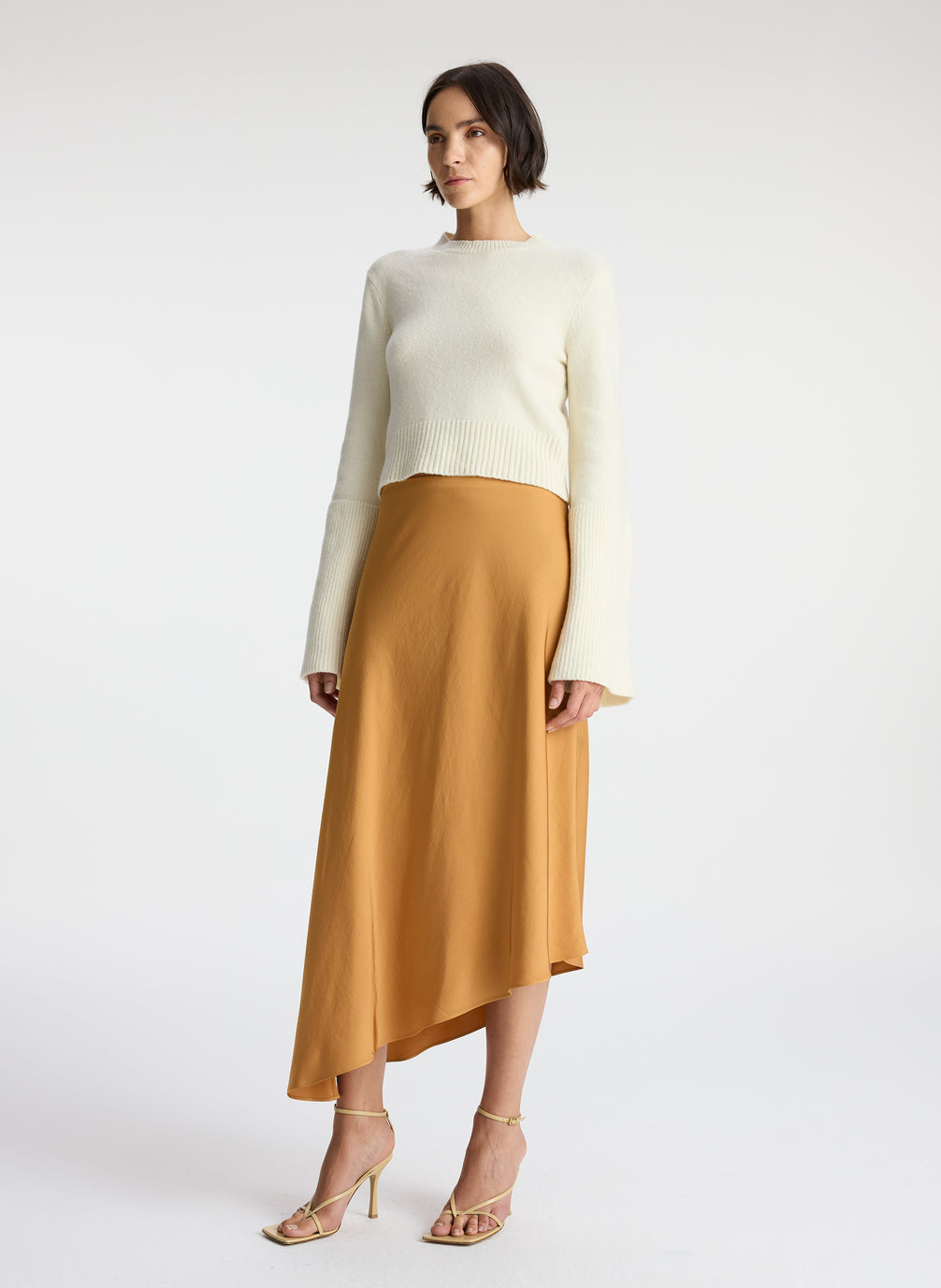 side view of woman wearing white sweater and brown satin asymmetric midi skirt