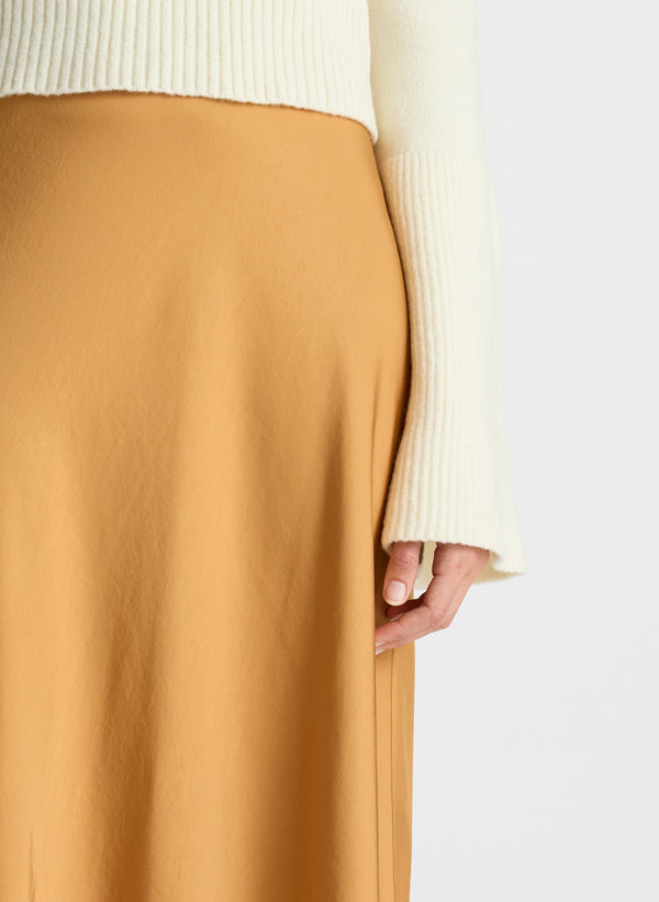 detail view of woman wearing white sweater and brown satin asymmetric midi skirt