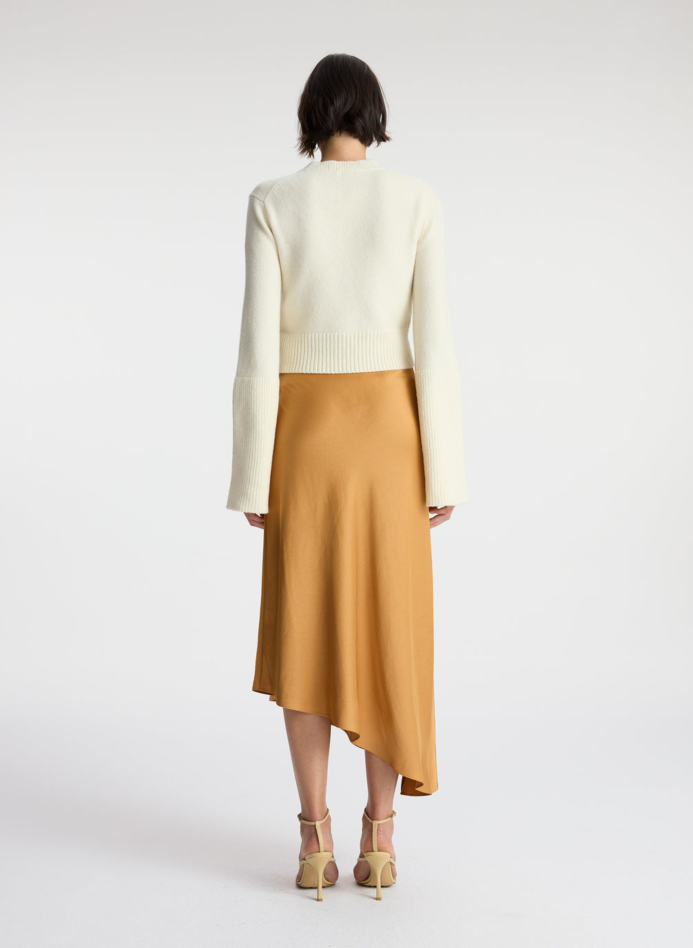 back view of woman wearing white sweater and brown satin asymmetric midi skirt