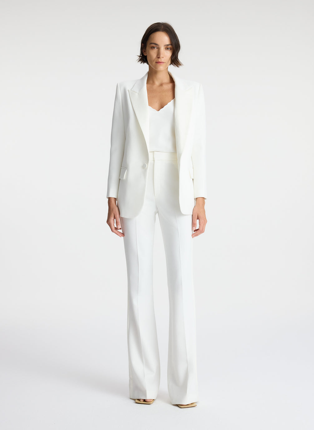 front view of woman wearing white blazer, white satin camisole, and white flared tuxedo pants