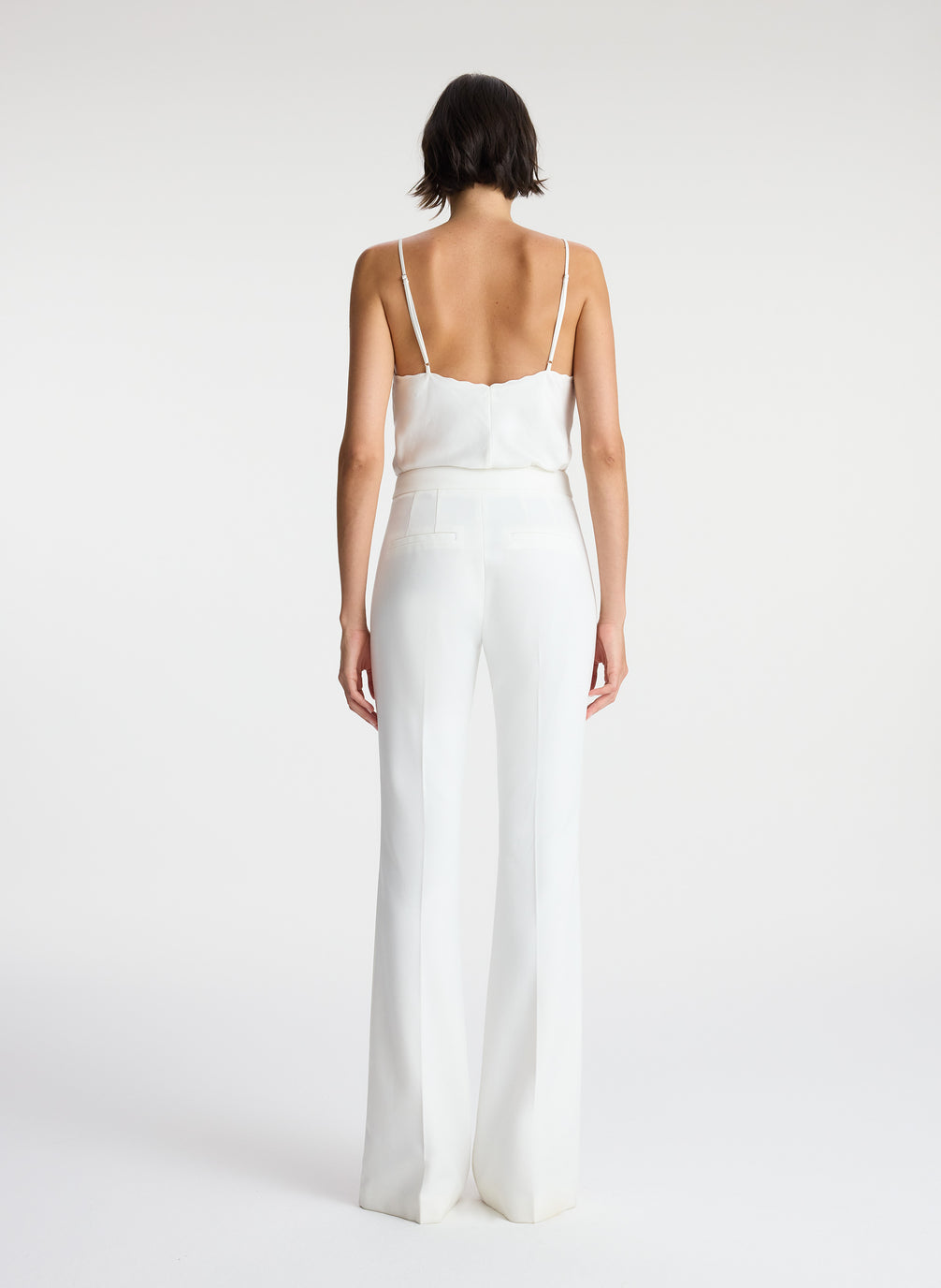 back view of woman wearing white satin camisole and white flared tuxedo pants