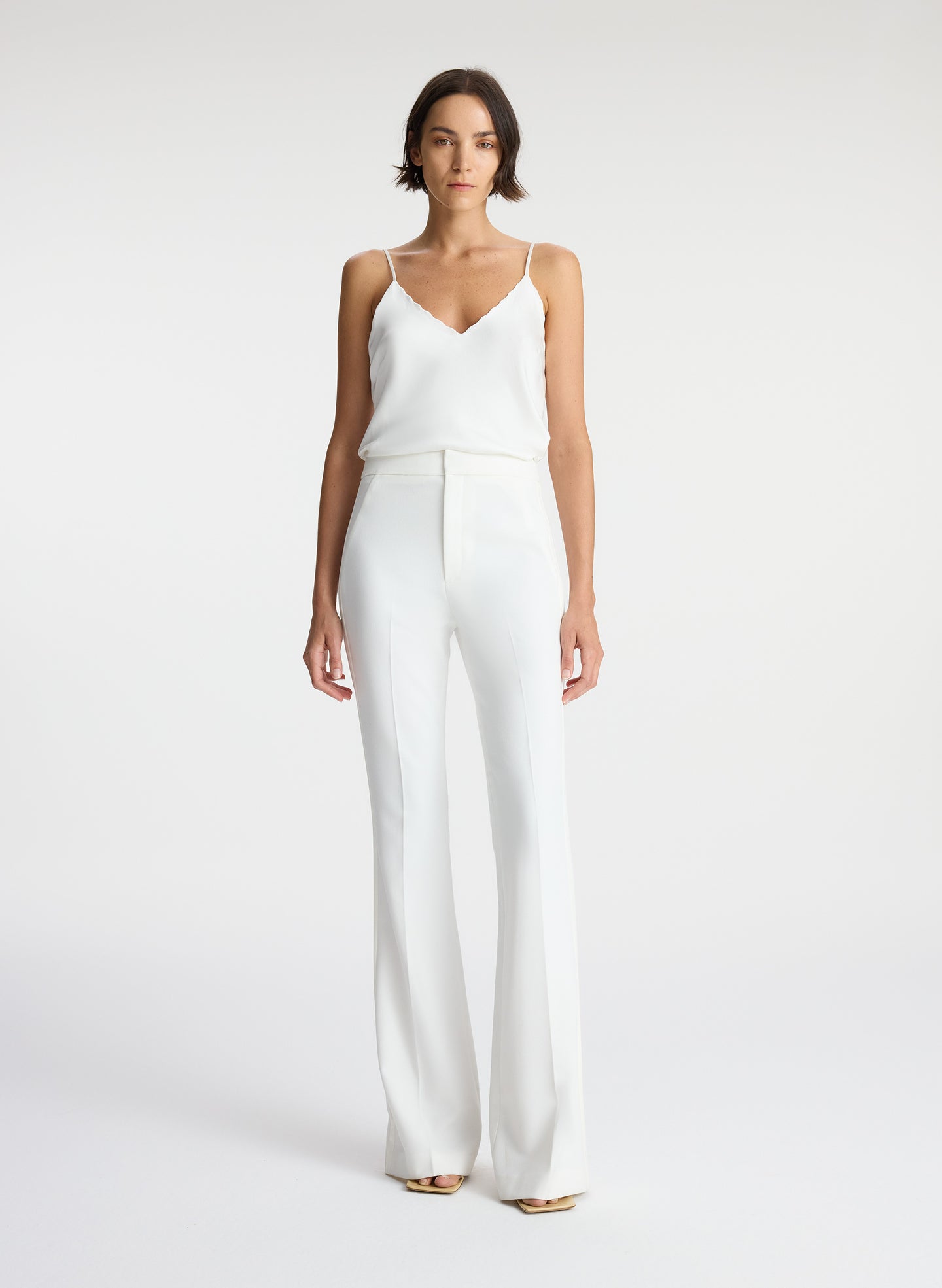 front view of woman wearing white satin camisole and white flared tuxedo pants