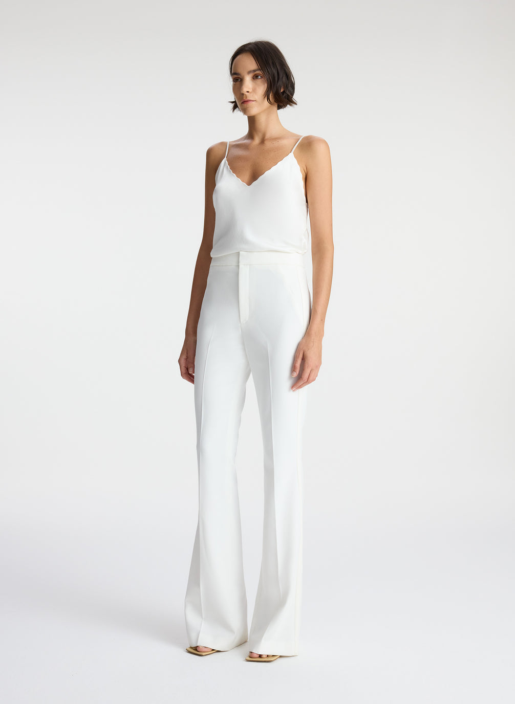 side view of woman wearing white satin camisole and white flared tuxedo pants