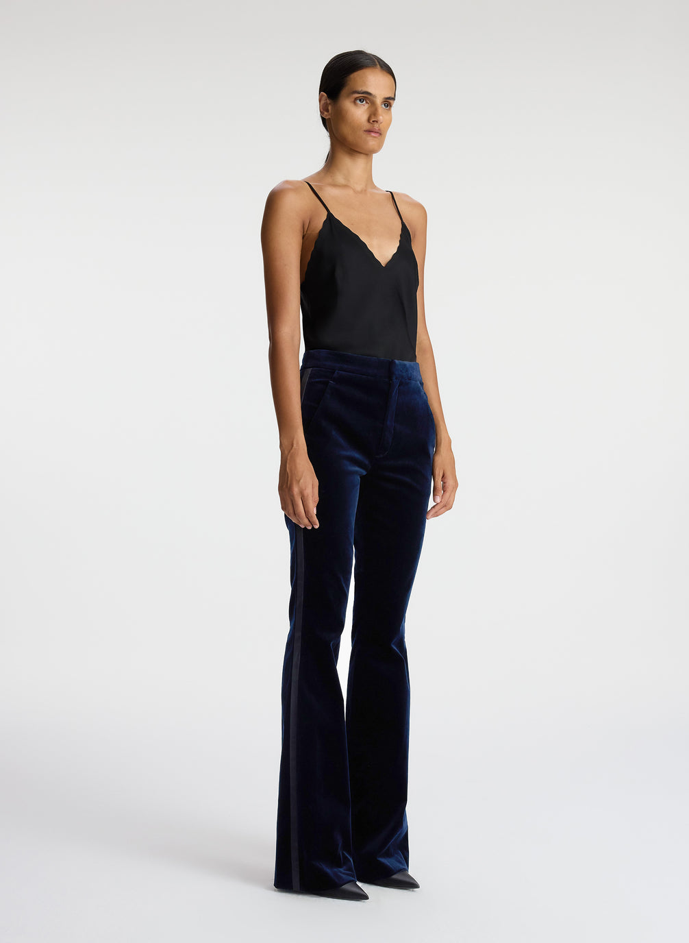 side view of woman wearing black satin camisole and navy blue velvet flared tuxedo pants