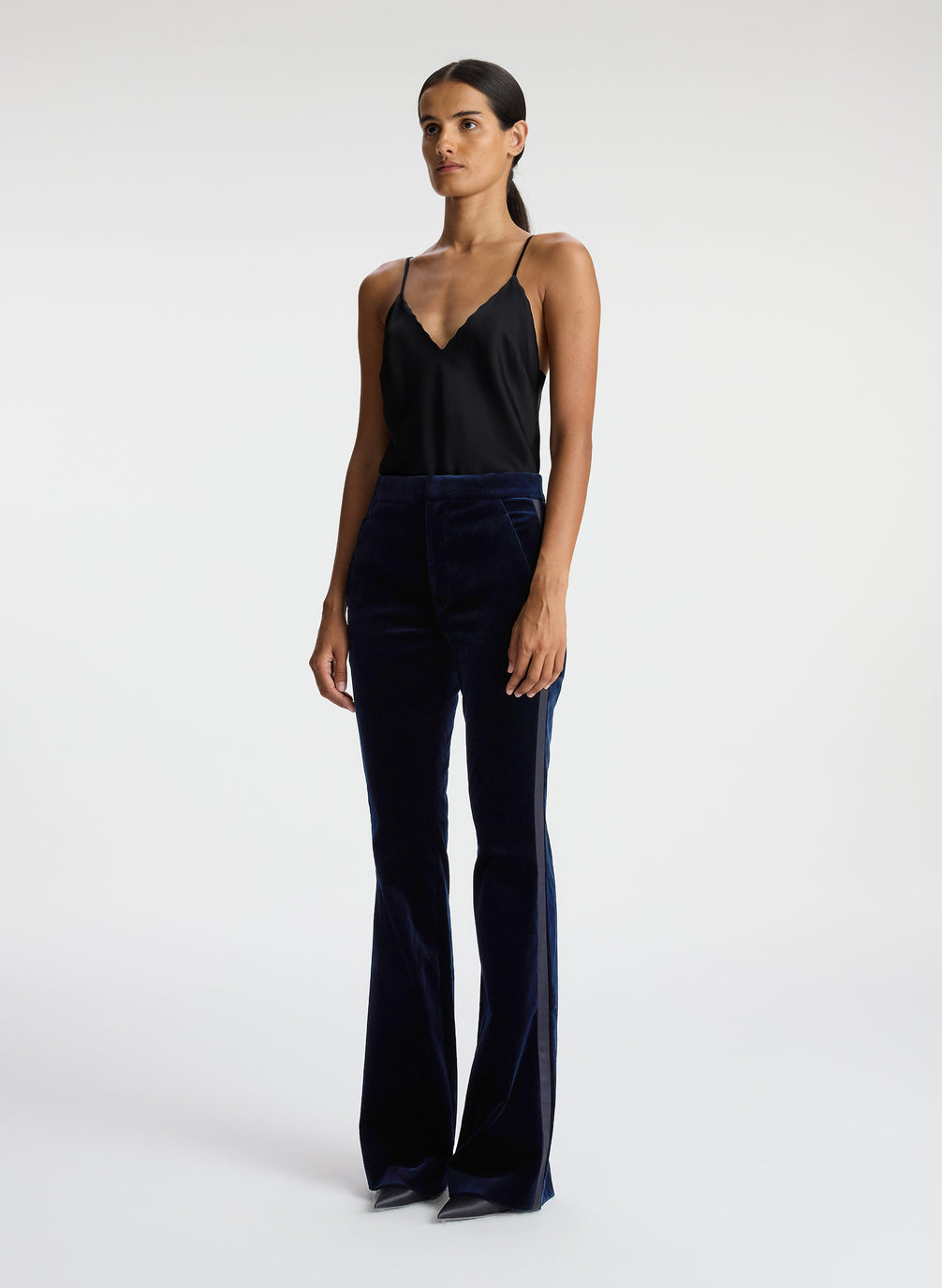 side view of woman wearing black satin camisole and navy blue velvet flared tuxedo pants