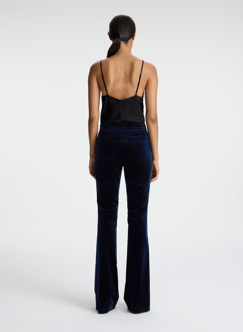 back view of woman wearing black satin camisole and navy blue velvet flared tuxedo pants
