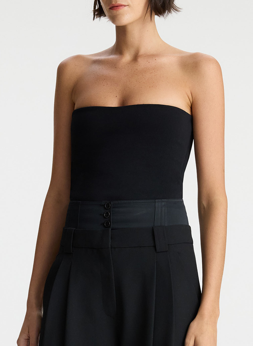 detail view of woman wearing black strapless compact knit top and black satin pants