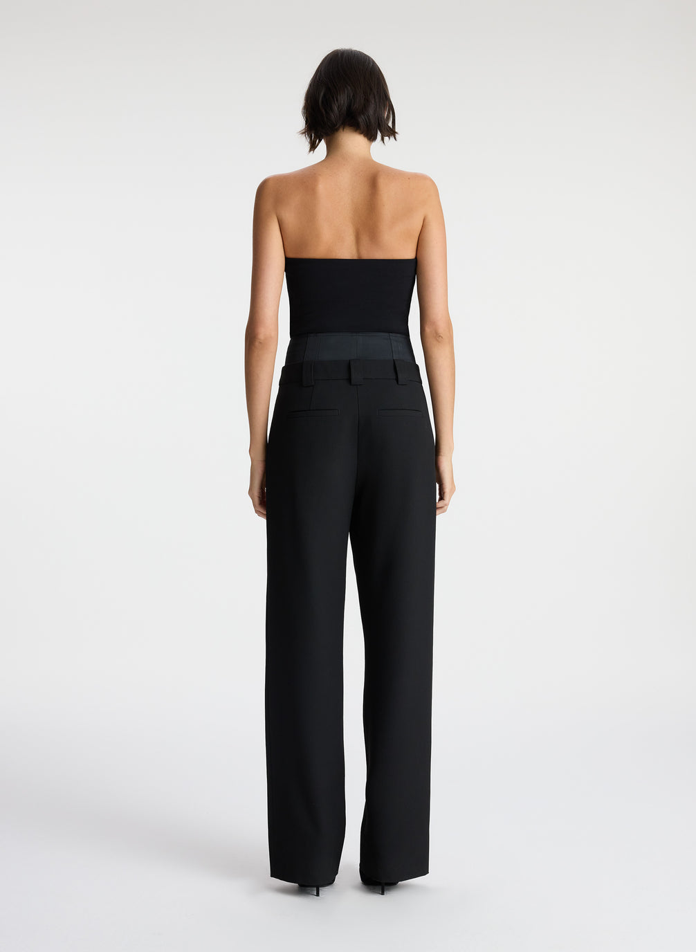 back view of woman wearing black strapless compact knit top and black satin pants
