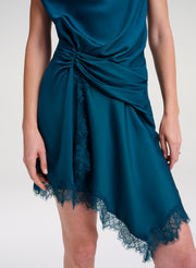 A close-up of a model wearing a teal satin wrap dress with a twisted waist detail and lace trim at the hem, set against a plain light gray background.