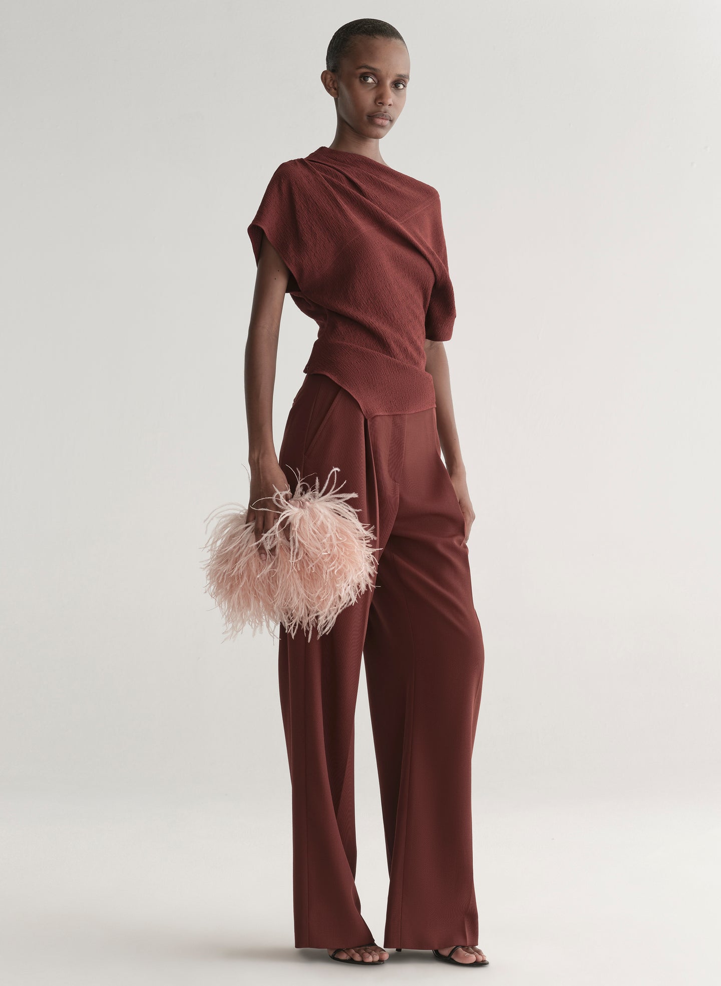 Model wearing a burgundy outfit with a feathered clutch against a light background