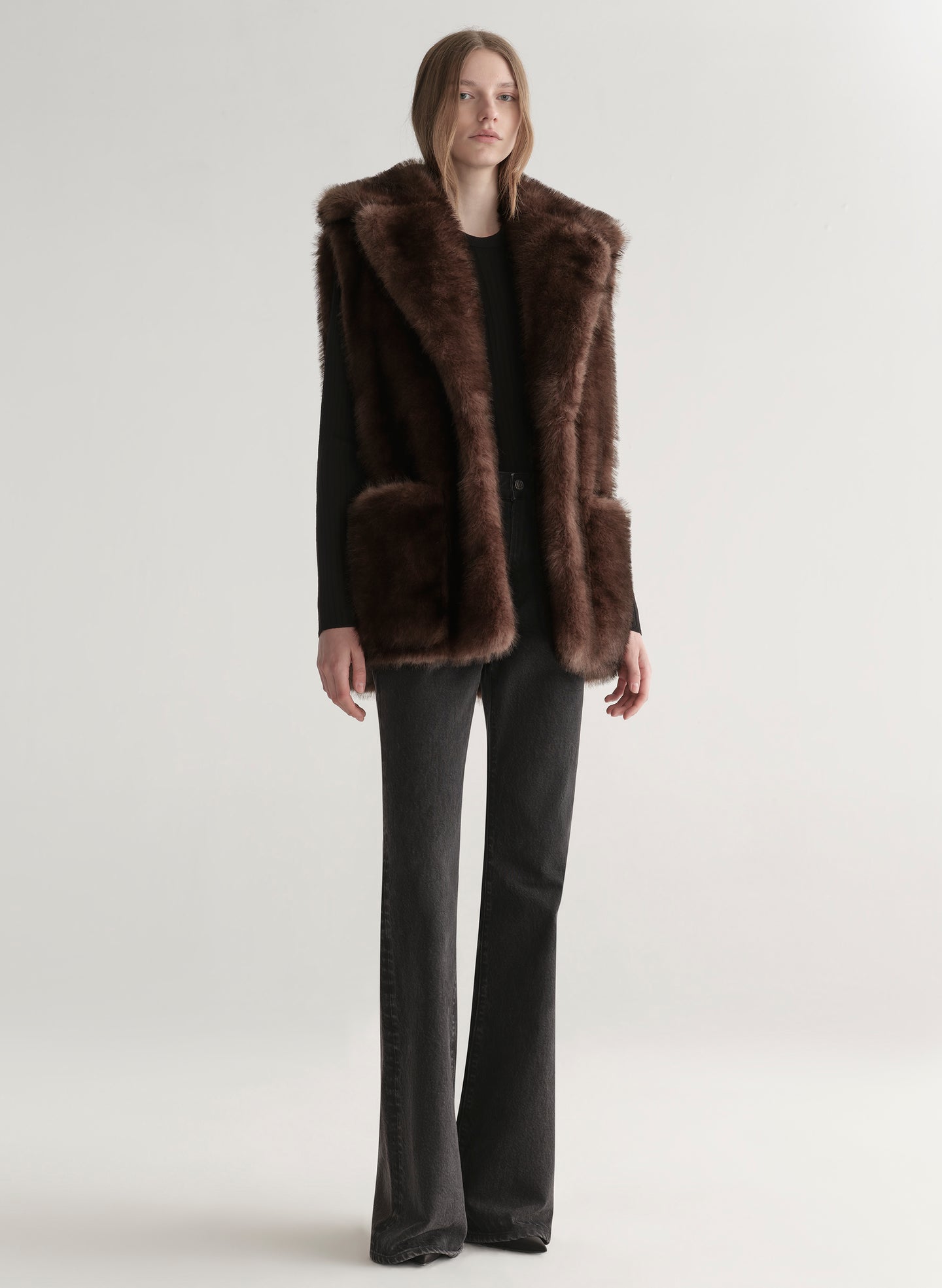 Model wearing a brown faux fur vest on a plain background