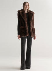 Model wearing a brown faux fur vest on a plain background
