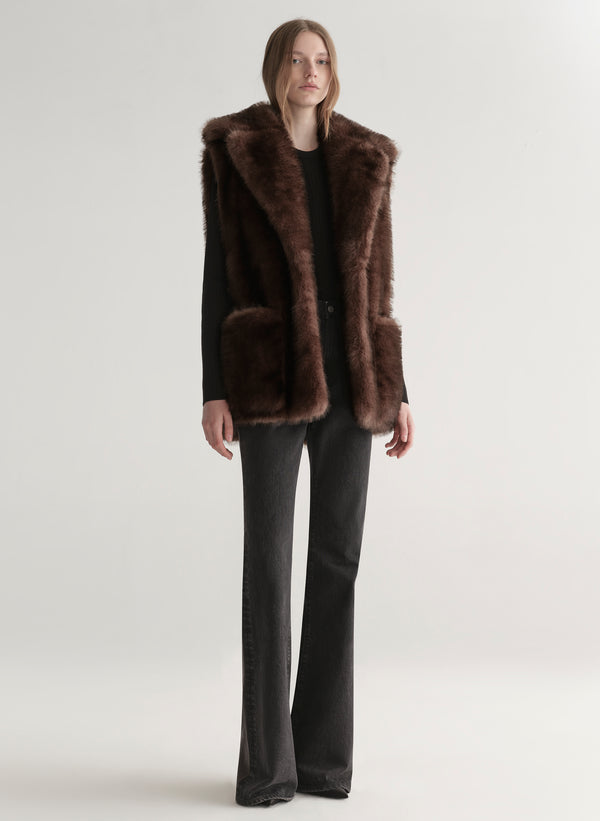 Model wearing a brown faux fur vest on a plain background