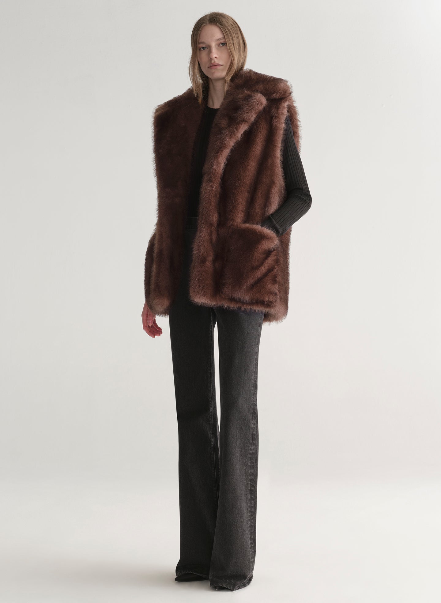 Model wearing a brown faux fur vest on a plain background