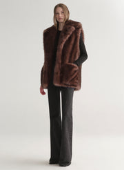 Model wearing a brown faux fur vest on a plain background