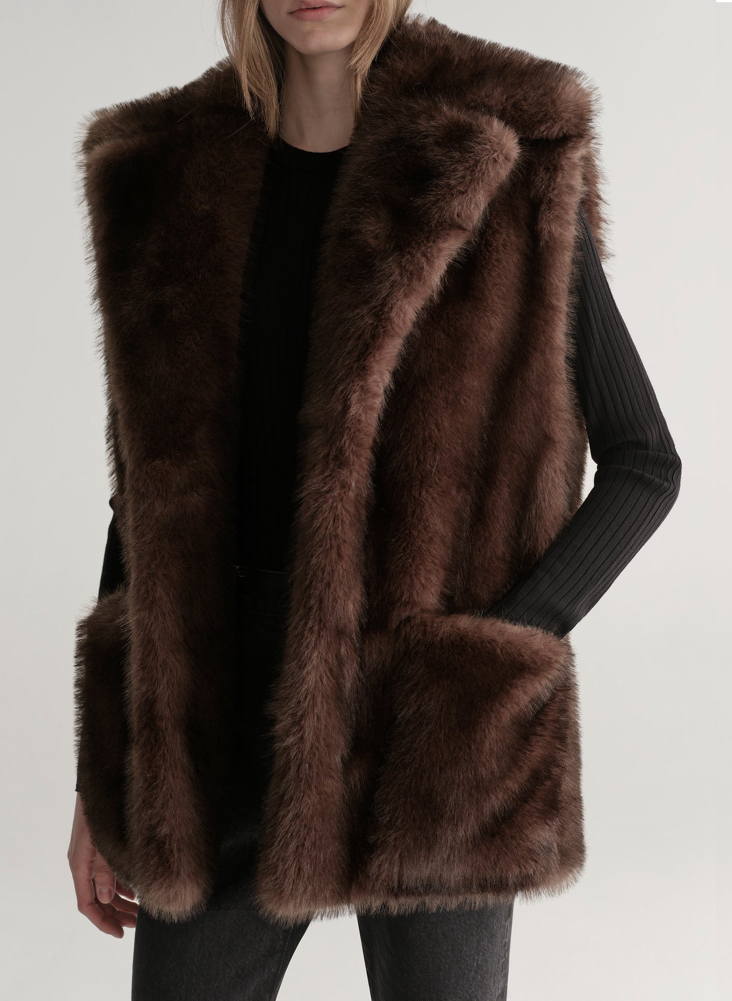 Model wearing a brown faux fur vest on a plain background
