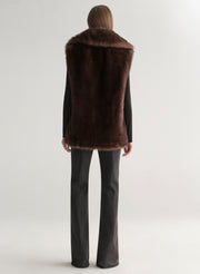 Model wearing a brown faux fur vest on a plain background