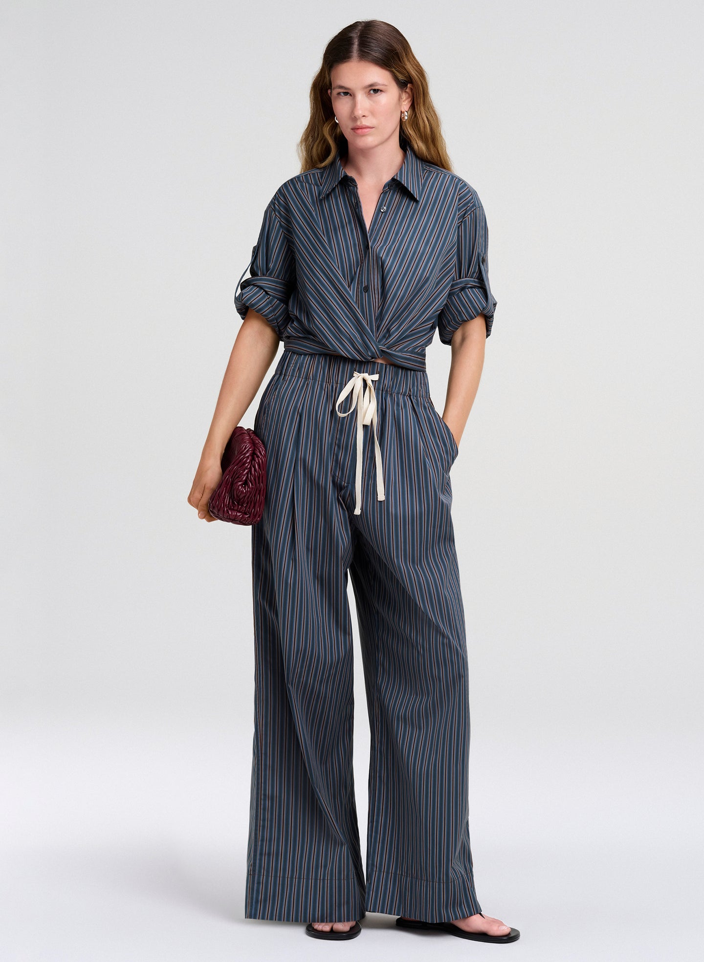 woman wearing blue striped top and pants carrying burgundy clutch bag