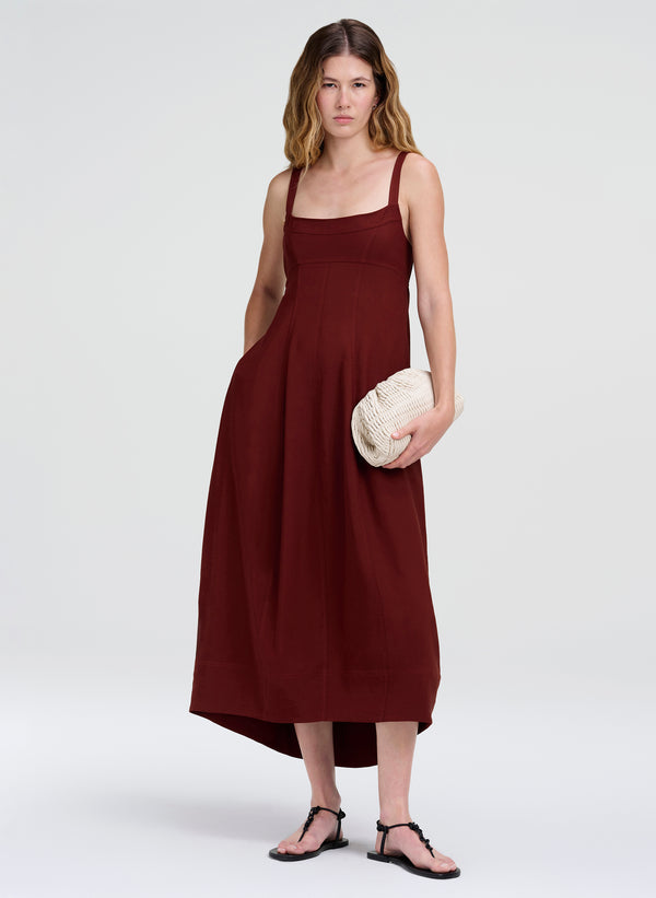 Woman wearing a burgundy dress holding a white clutch against a white background