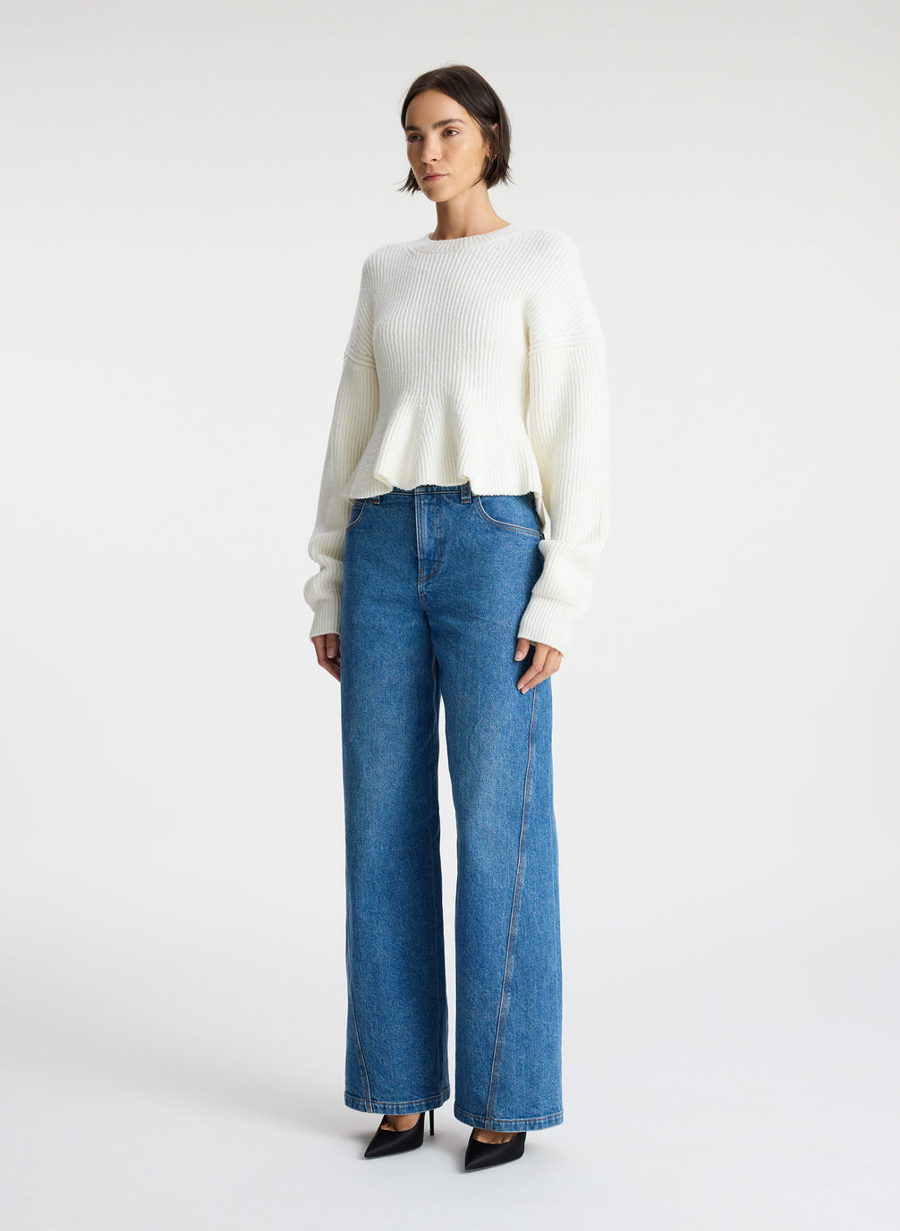 side view of woman wearing white peplum sweater and medium blue wash denim jeans