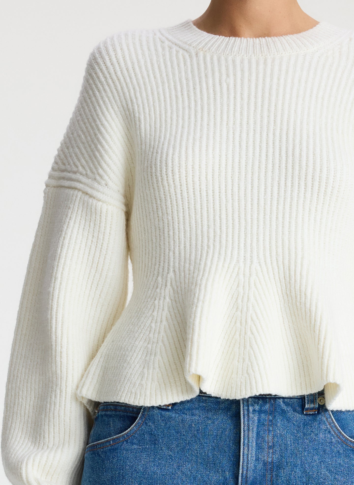 detail view of woman wearing white peplum sweater and medium blue wash denim jeans
