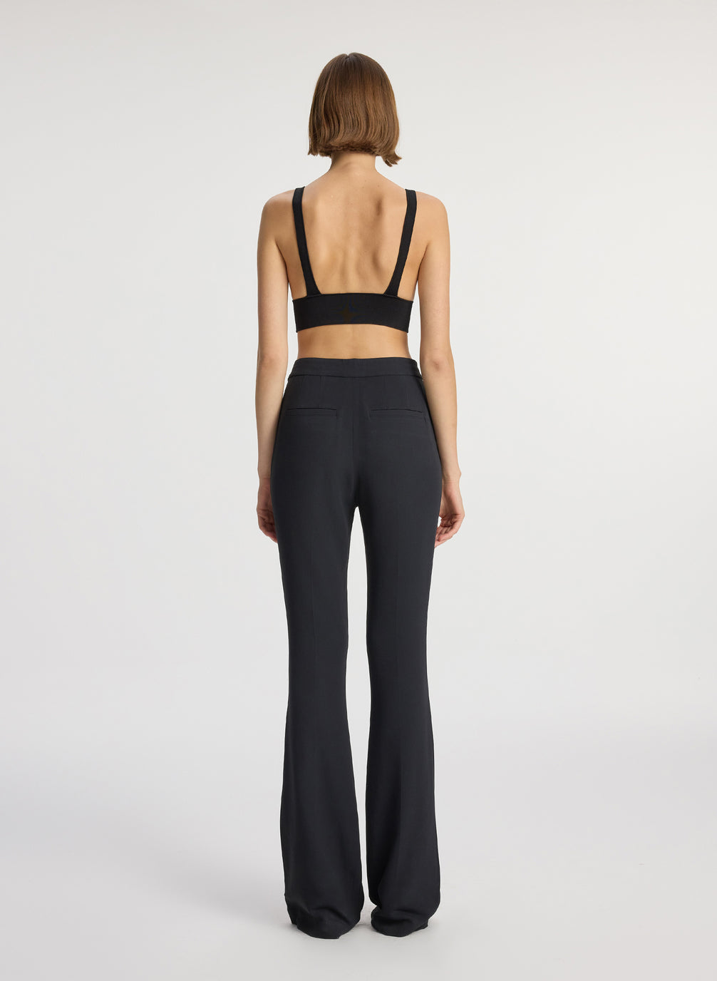 back view of woman wearing black knit bra and black flared pants