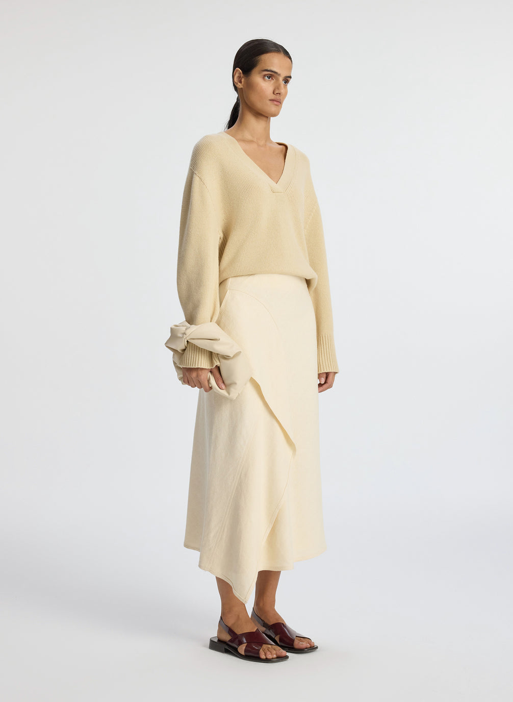 side view of woman wearing beige v neck sweater and cream skirt