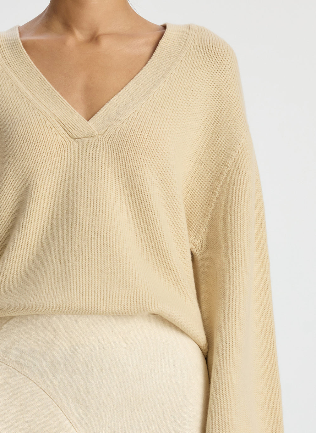 detail view of woman wearing beige v neck sweater and cream skirt