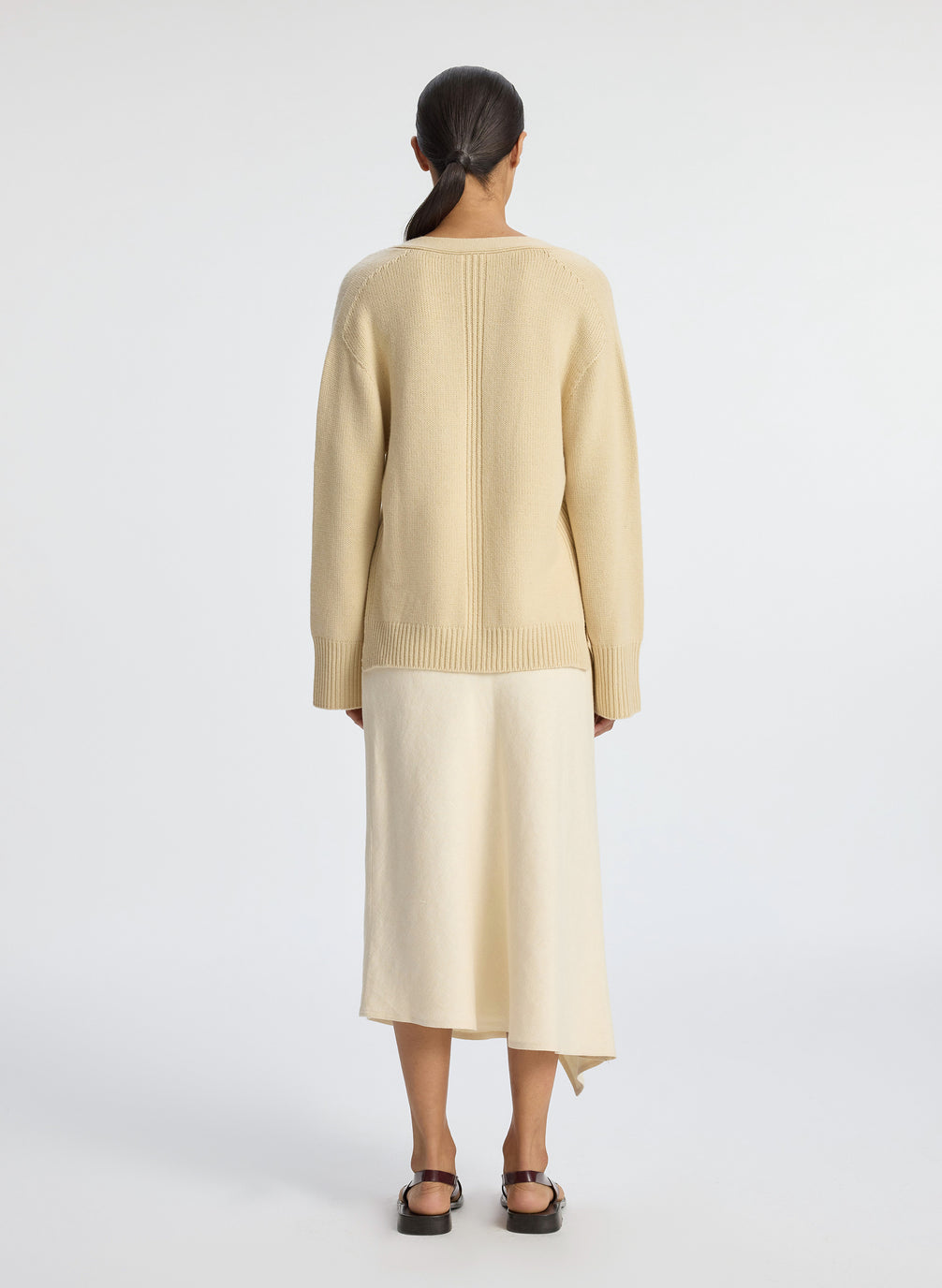 back view of woman wearing beige v neck sweater and cream skirt