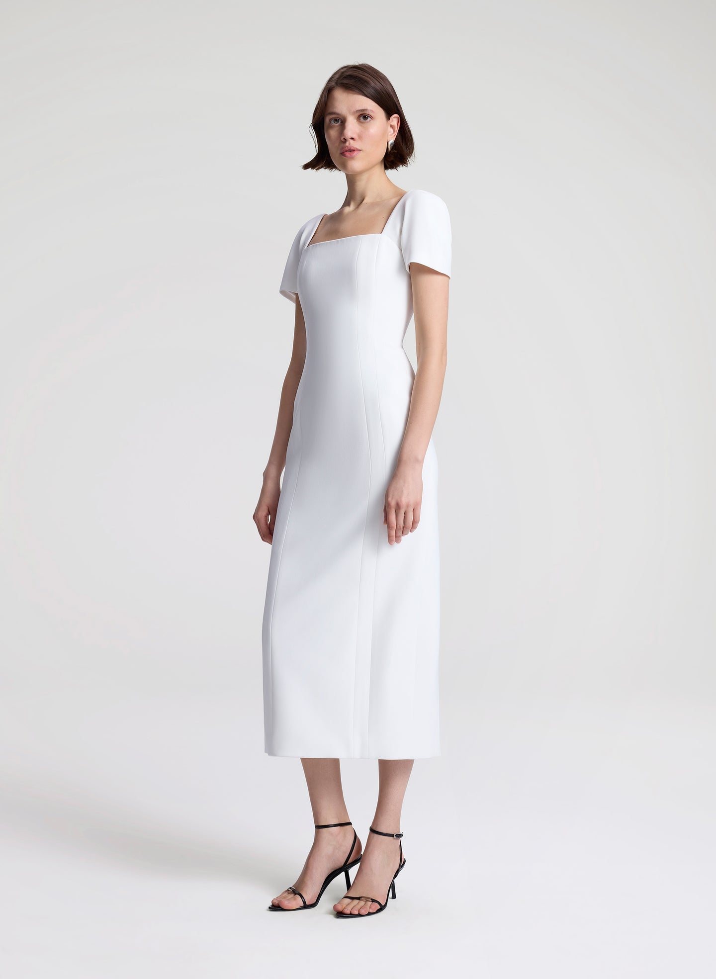 Woman wearing a white midi dress on a plain background