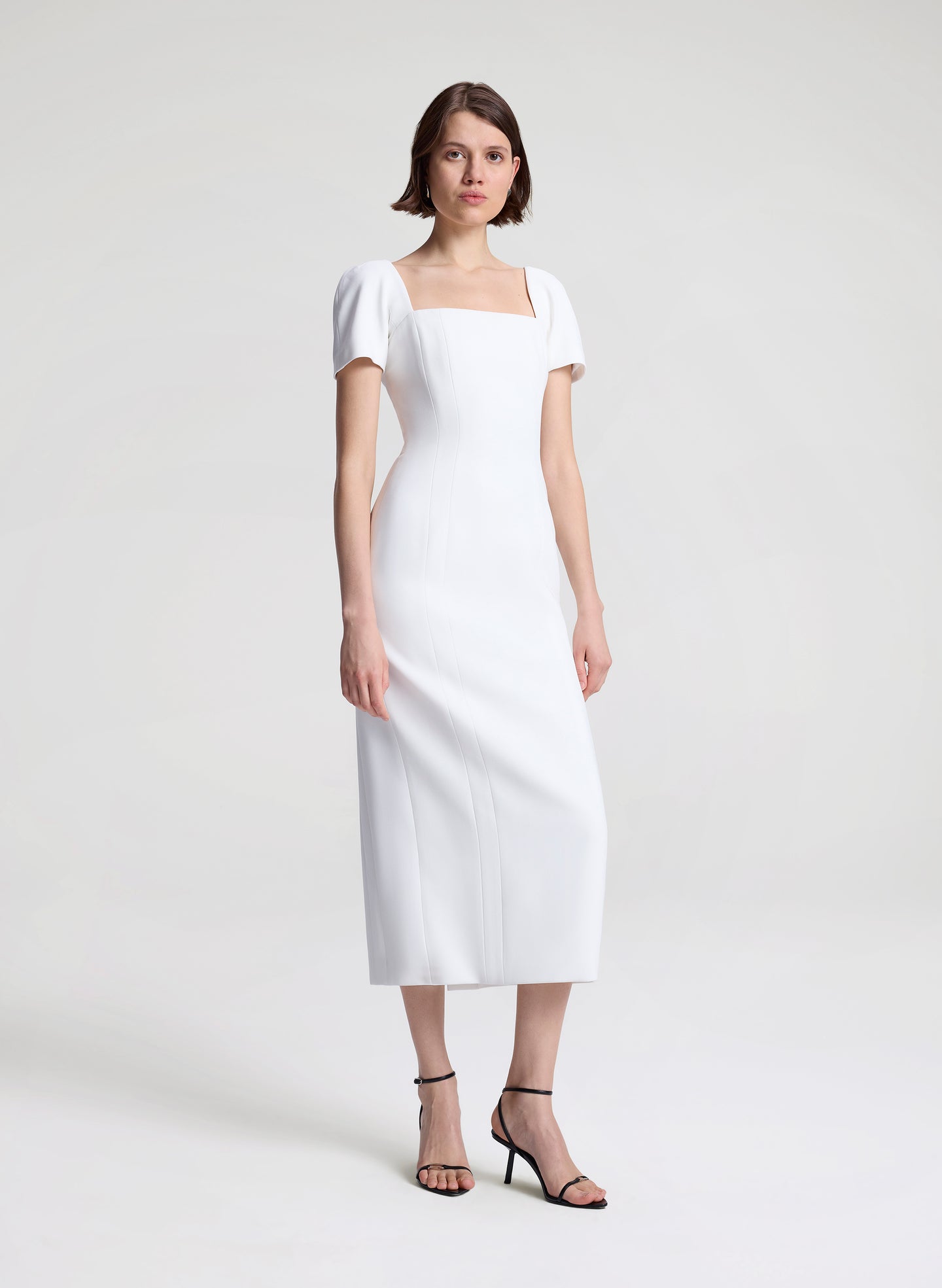 Woman wearing a white midi dress on a plain background