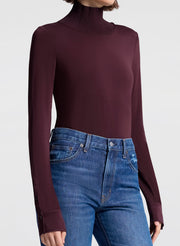 Person wearing a dark purple turtleneck sweater and blue jeans on a white background