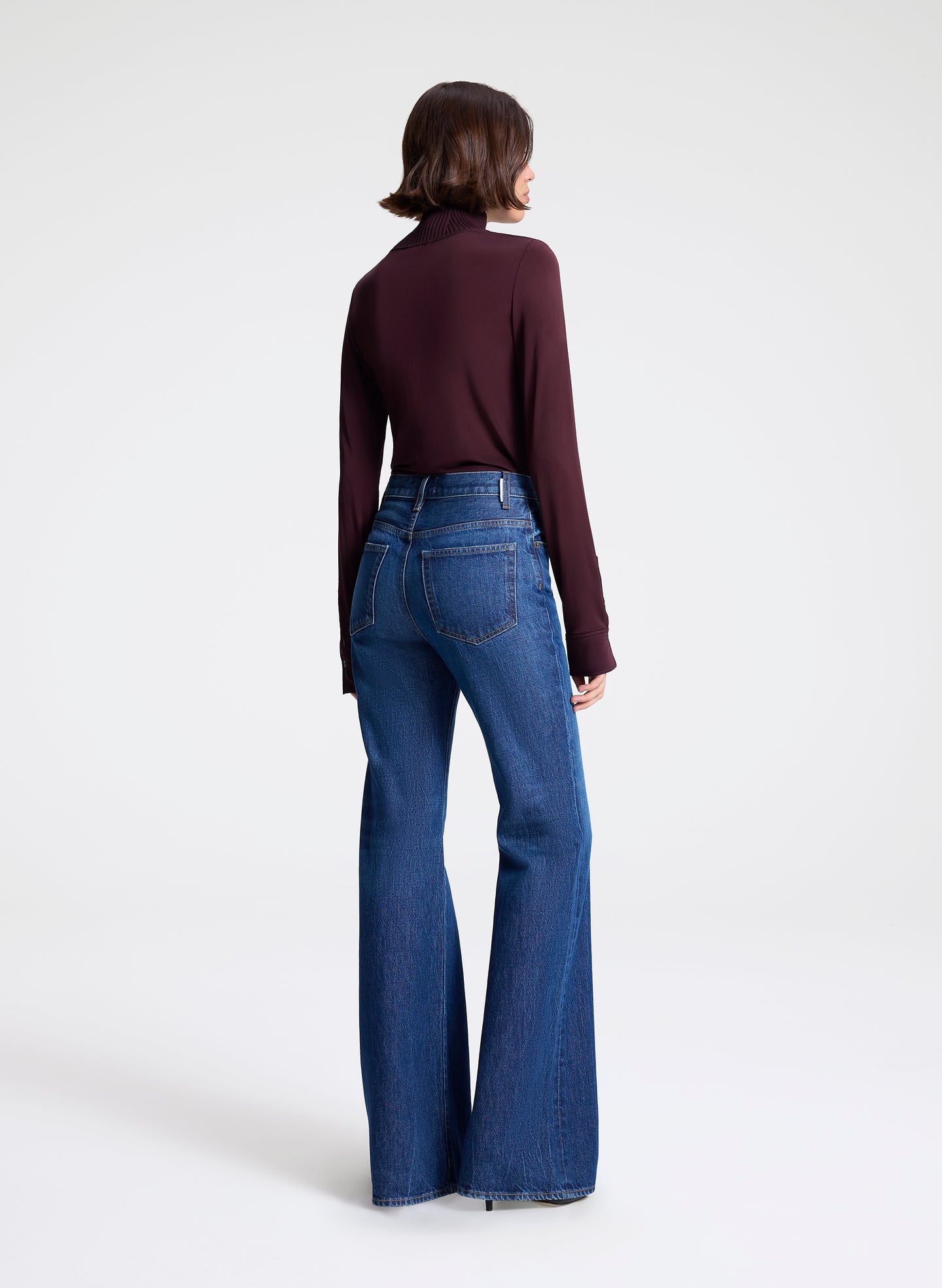 Person wearing a dark purple top and blue flared jeans on a white background