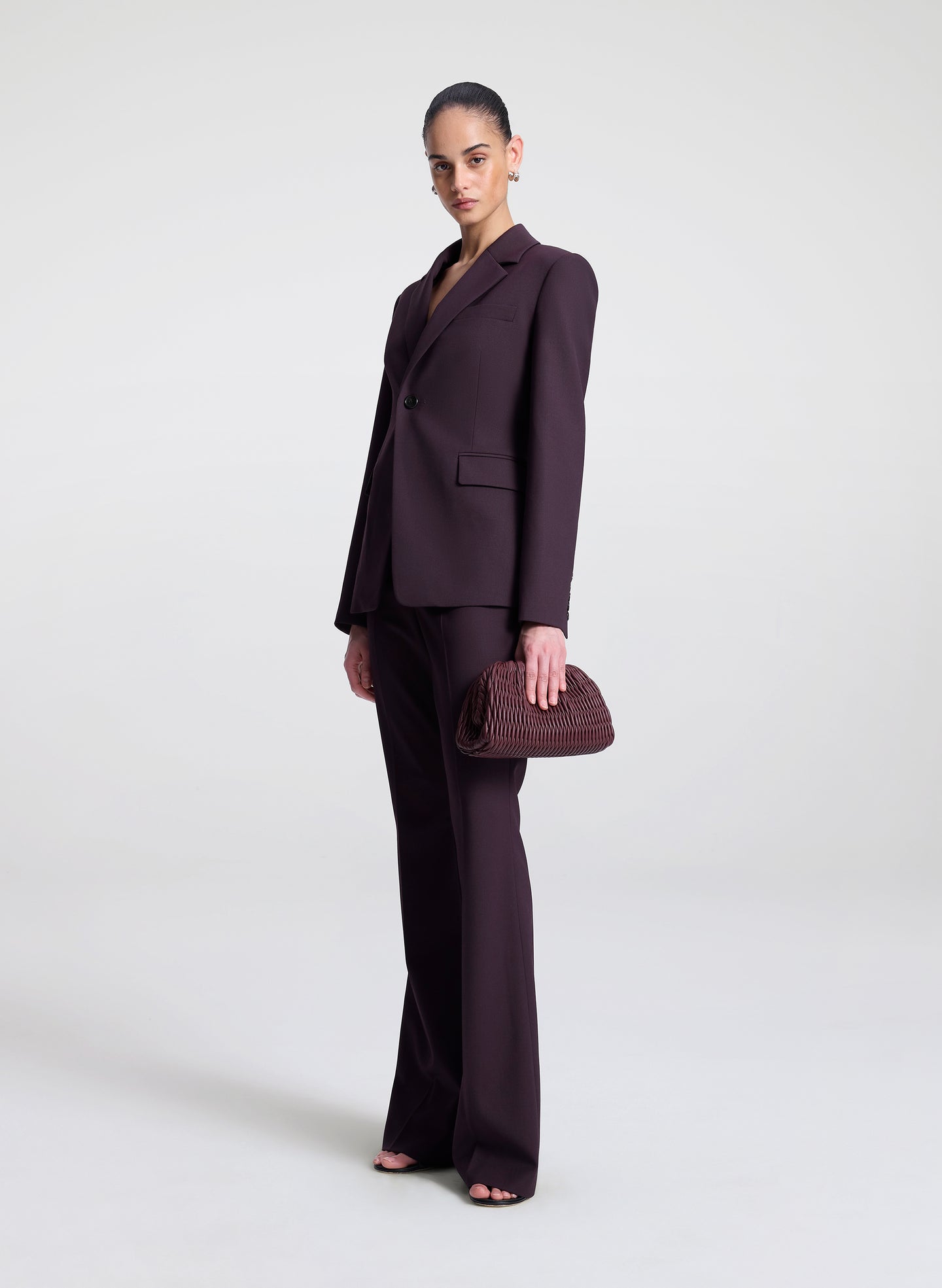 Woman wearing a dark purple suit holding a matching clutch against a white background