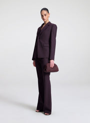 Woman wearing a dark purple suit holding a matching clutch against a white background