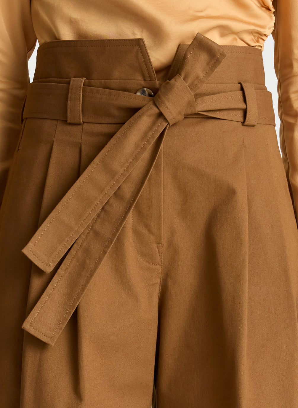 detail view of woman wearing tan one shoulder long sleeve top and brown wide leg pants