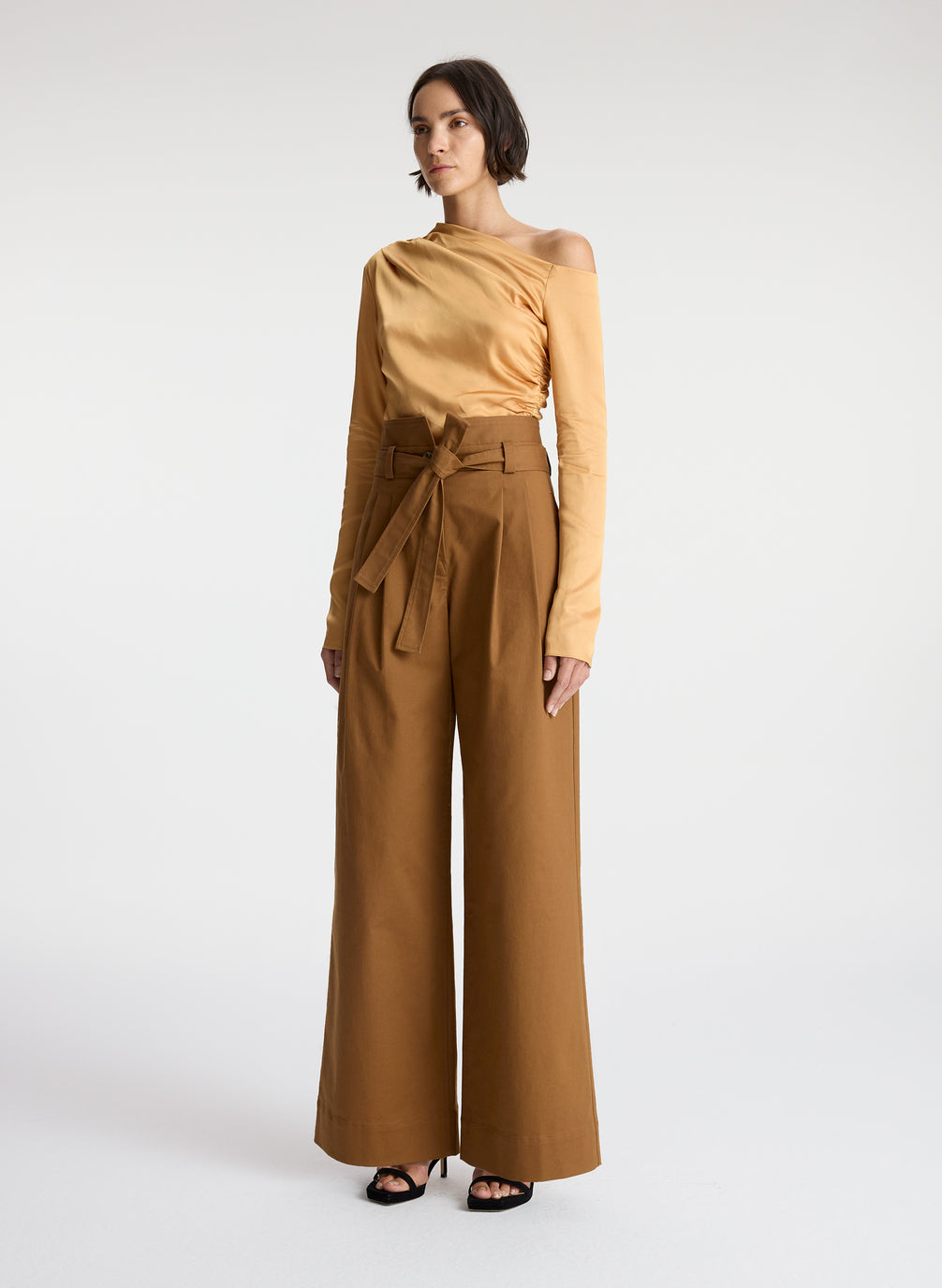 side view of woman wearing tan one shoulder long sleeve top and brown wide leg pants