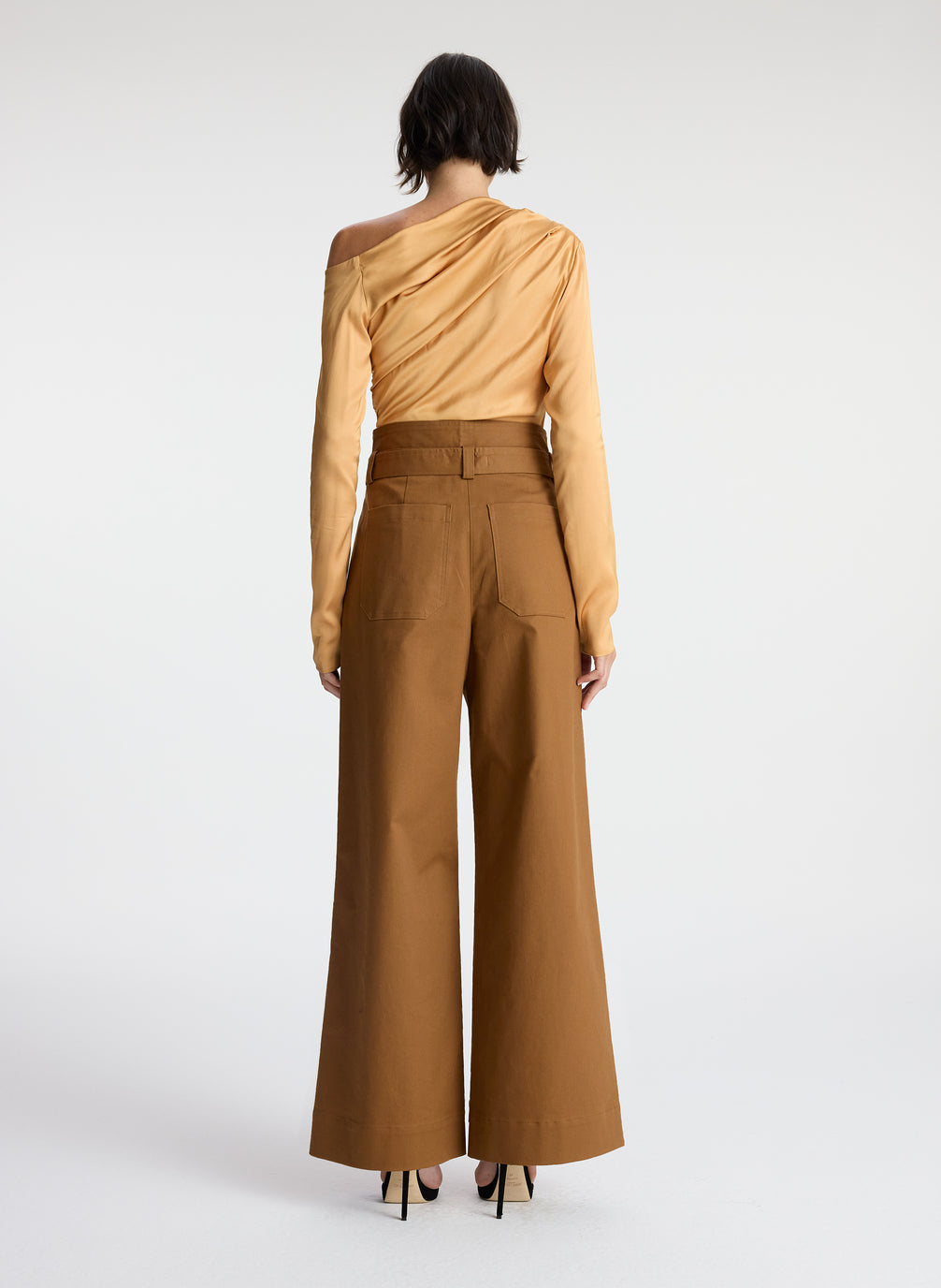 back view view of woman wearing tan one shoulder long sleeve top and brown wide leg pants