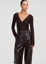A model wearing a dark brown long-sleeve wrap top and matching dark brown leather wide-leg pants, photographed against a light gray studio background.