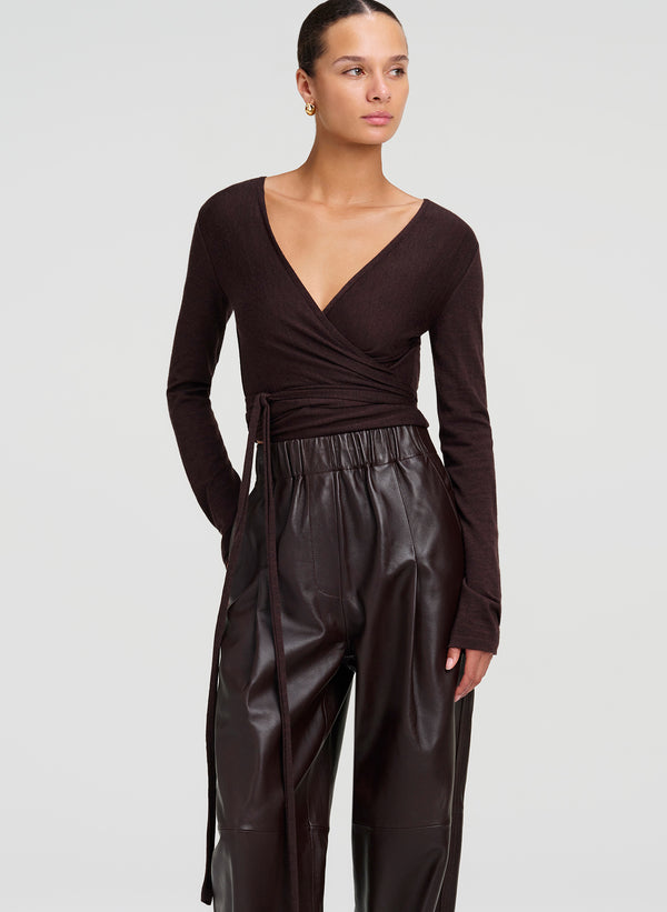A model wearing a dark brown long-sleeve wrap top and matching dark brown leather wide-leg pants, photographed against a light gray studio background.