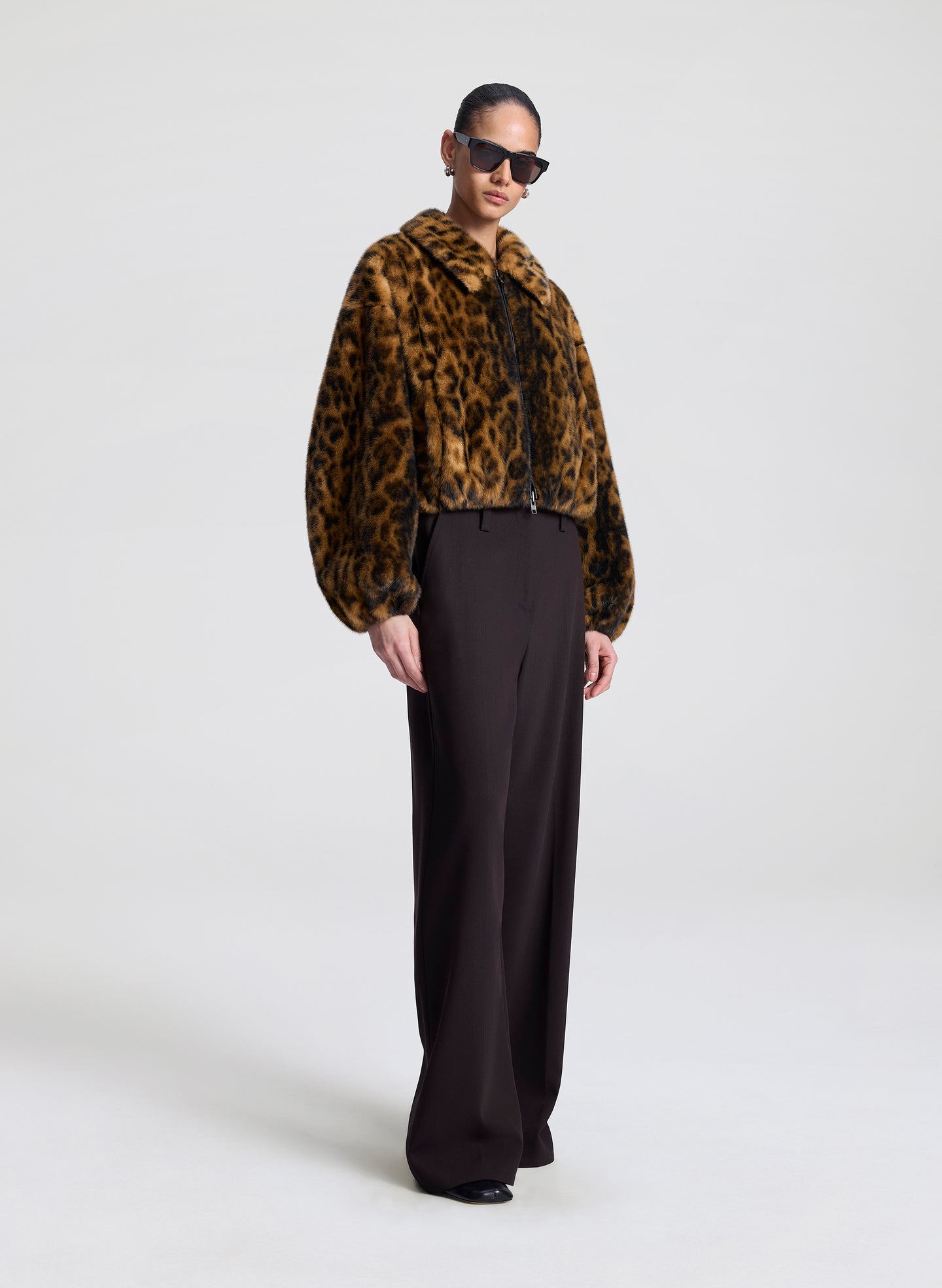 Person wearing a leopard print jacket and black pants on a white background